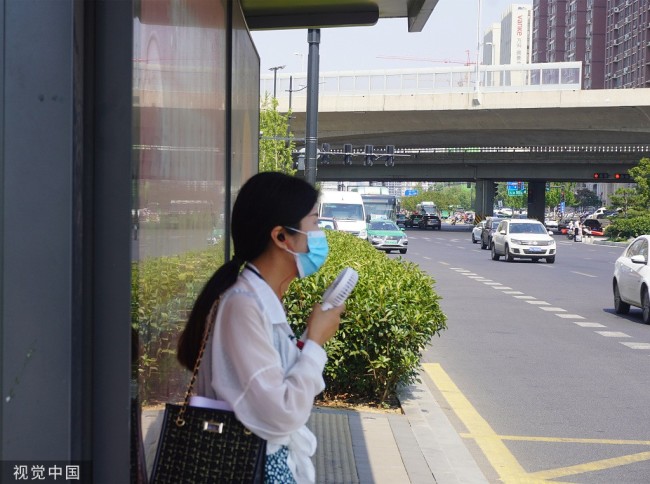 2022年6月16日，郑州，在公交站台候车的市民用电动小风扇吹风。当日，郑州市气象台发布高温红色预警信号。 中新社记者 刘鹏 摄