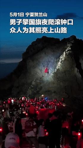 男子举国旗夜爬石头山众人为他打光 山顶飘扬引欢呼