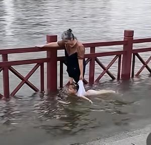 温馨又危险！老人手扶栏杆提着女孩在江边游泳