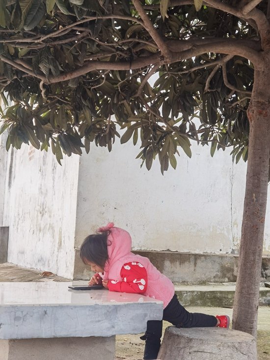 中部省份某村庄，一名小女孩独自在玩手机。