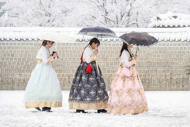 2024年11月27日，韩国首尔，游客们身穿传统韩服，在景福宫内观赏雪景。视觉中国 图