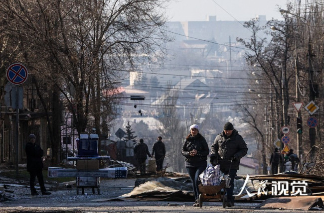当地时间2022年4月5日，乌克兰马里乌波尔，当地民众在被炮弹摧毁的建筑附近行走。