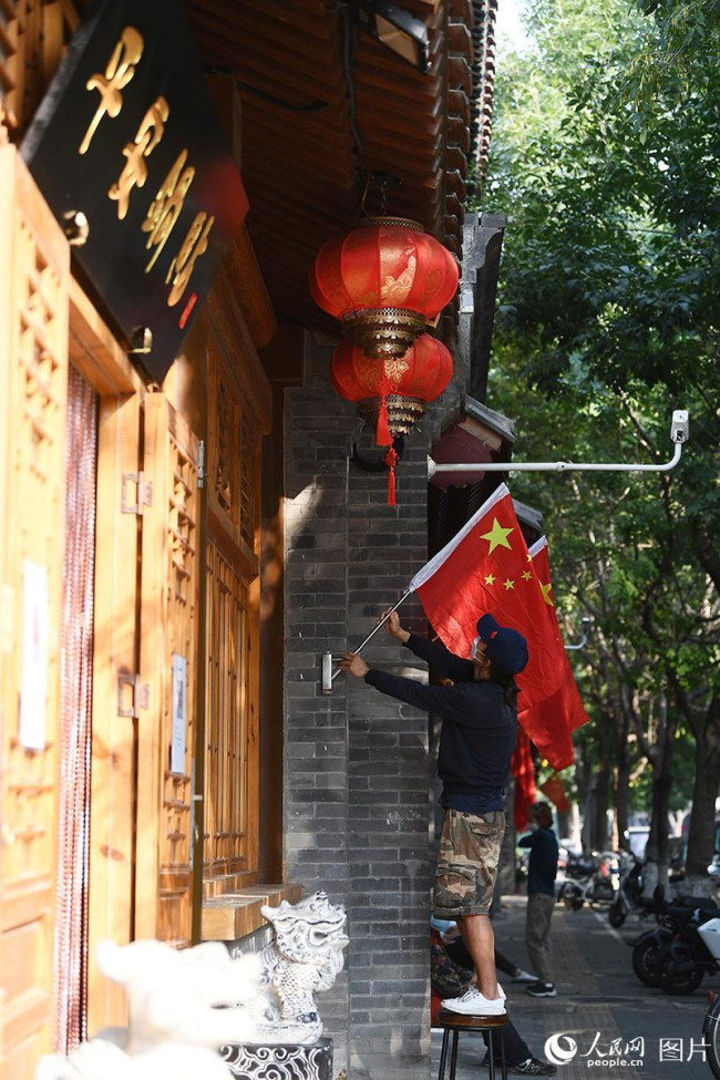 9月30日，北京西兴隆街，临街商家工作人员正在悬挂国旗迎接国庆的到来。人民网记者 于凯摄