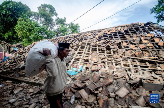 11月22日，在印度尼西亚西爪哇省展玉地区，一名男子从被地震损坏的房屋前走过。